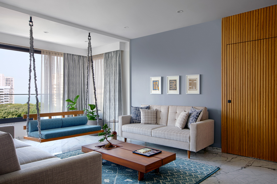 Nautical family room design with wood door and coffee table, swing in front of big window, off-white couches