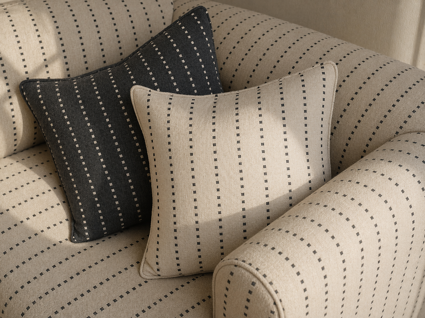 Beige upholstered sofa with subtle dashed stripe fabric, styled with coordinated light and charcoal patterned cushions for a layered contemporary look - Beautiful Homes