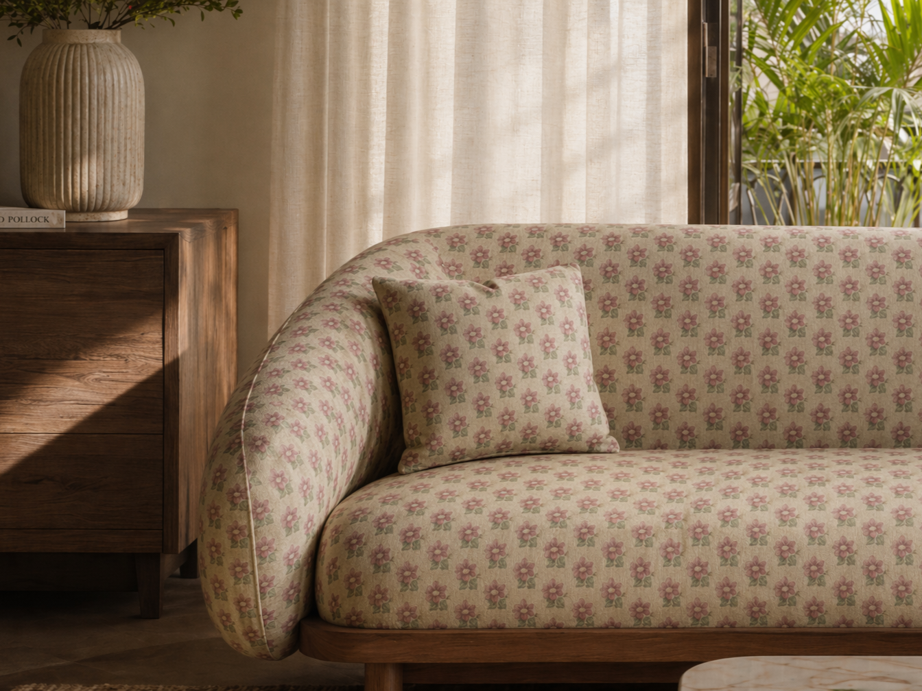 Curved sofa with cream floral upholstery, rounded armrest, and matching cushion, styled beside a dark wood cabinet - Beautiful Homes