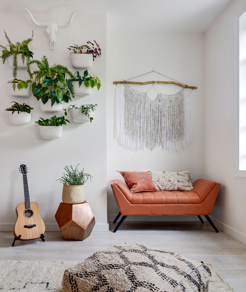 A corner of a room with a bench covered in orange fabric and some plants hanging on the wall - Beautiful Homes
