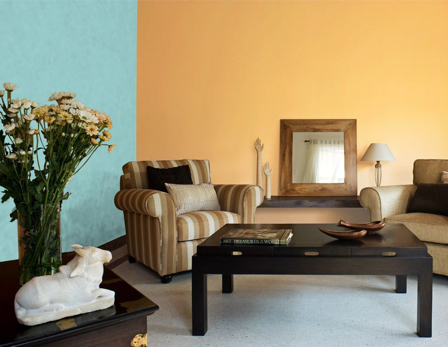 A living room painted in blue and yellow with two chairs and a large wooden centre table - Beautiful Homes