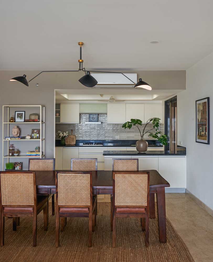 A six seater dining table with rattan chairs and behind it is a kitchen - Beautiful Homes
