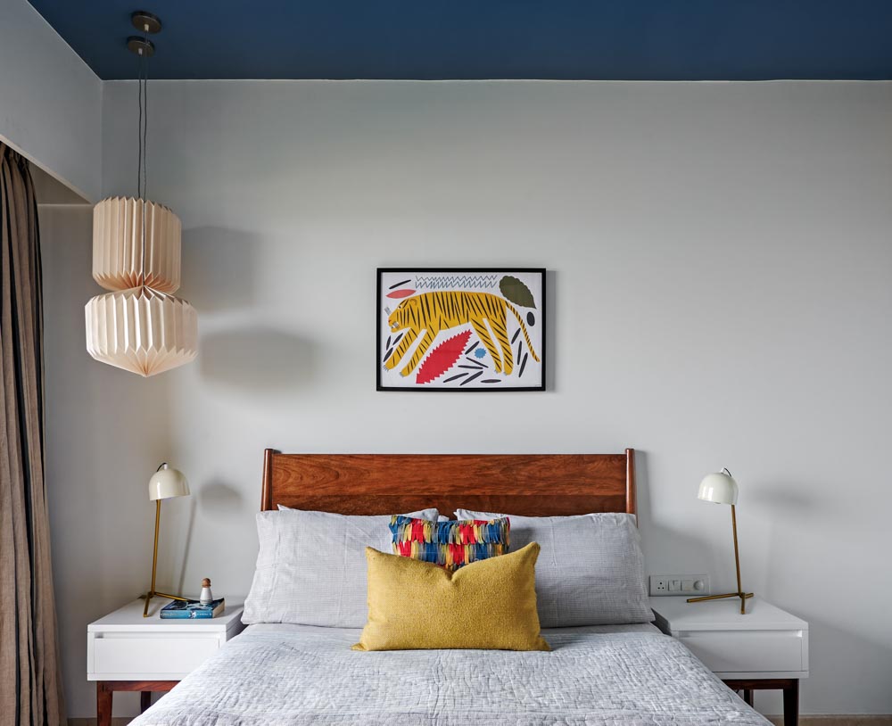 A white bedroom with blue roof, a bed with wooden headboard and an artwork placed on the wall - Beautiful Homes